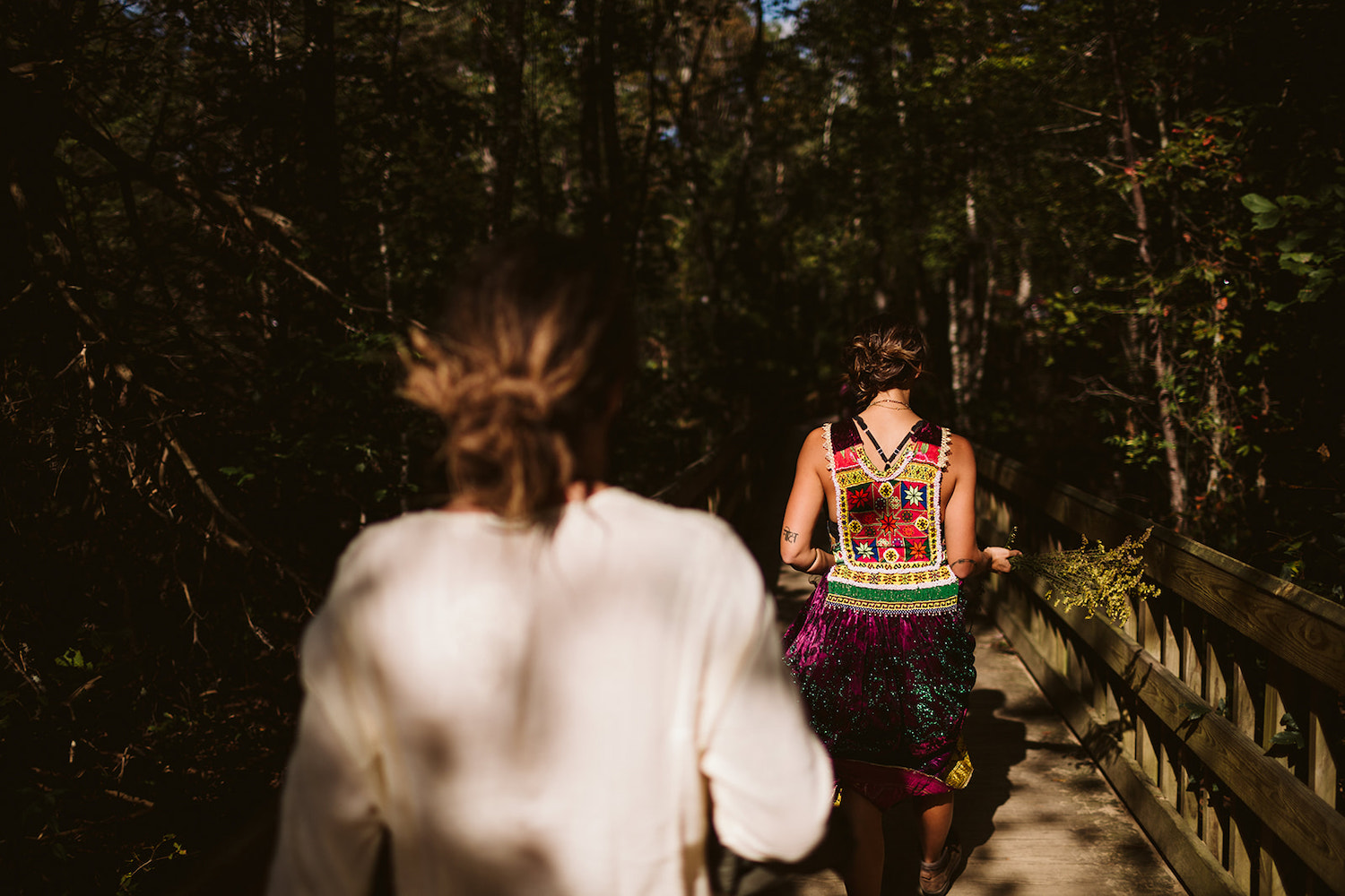 man and woman in colorful Bohemian dress cross a wooden bridge