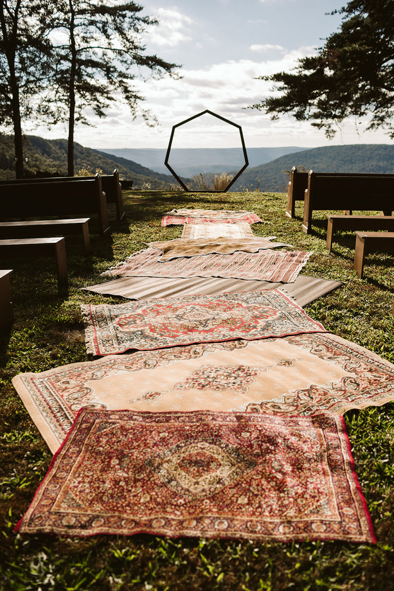 multi-colored Oriental rugs line aisle between benches leading to a heptagon arch at Hemlock Falls Bohemian festival wedding