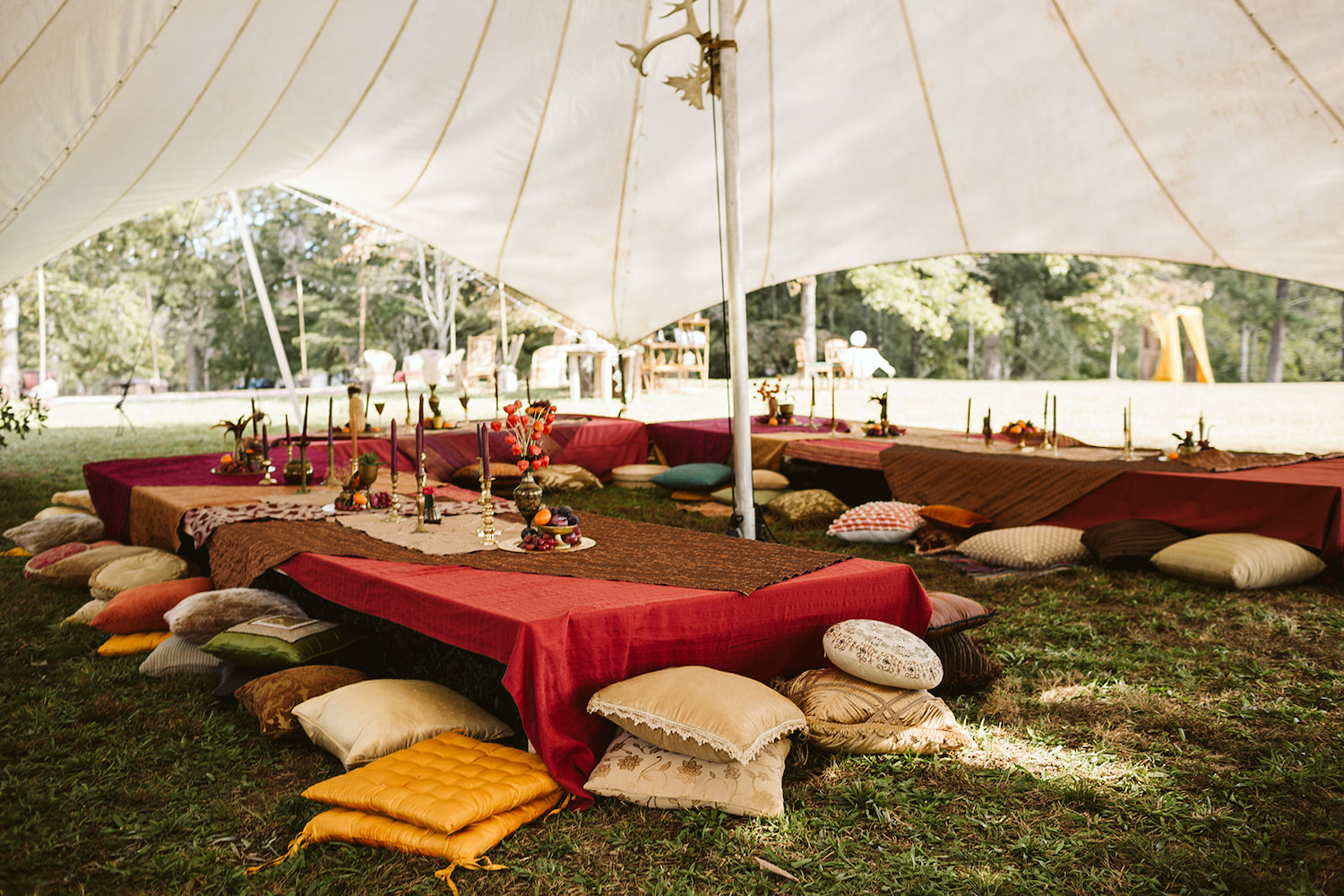 low tables covered with bright cloths and surrounded by colorful pillows sit under white tent at Bohemian festival wedding