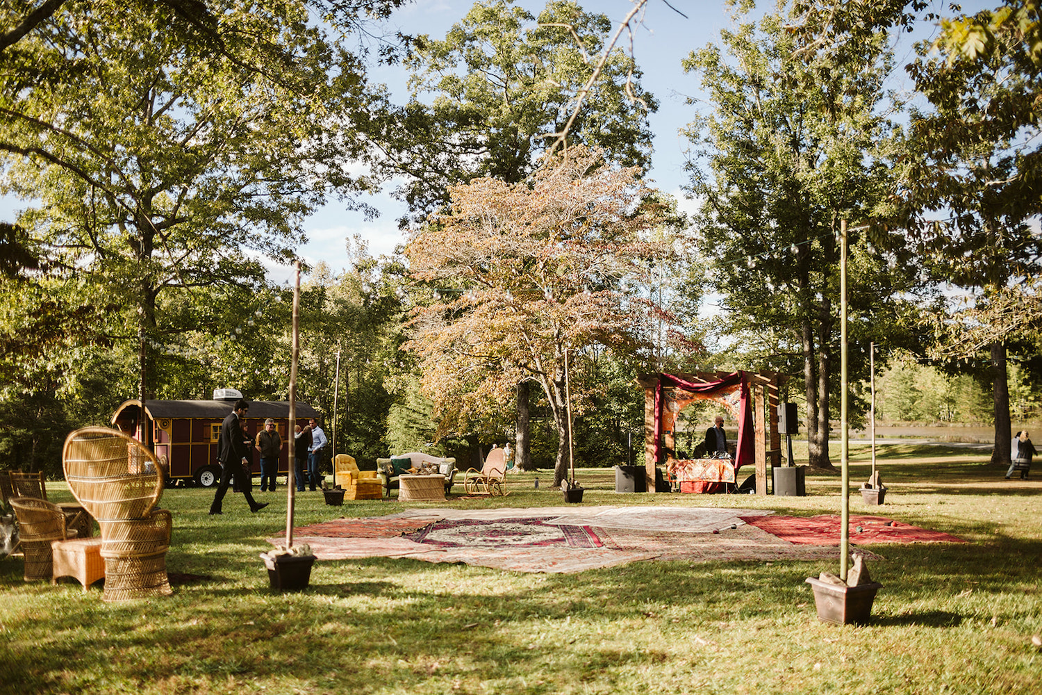 set up for Bohemian festival wedding with multiple Oriental rugs near gypsy wagon and wicker furniture sets