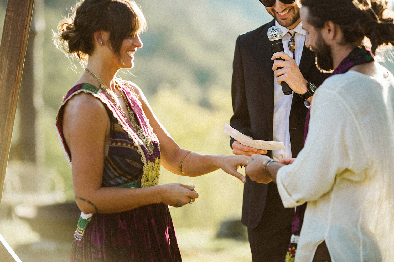 man places ring on woman's hand while they smile at each other