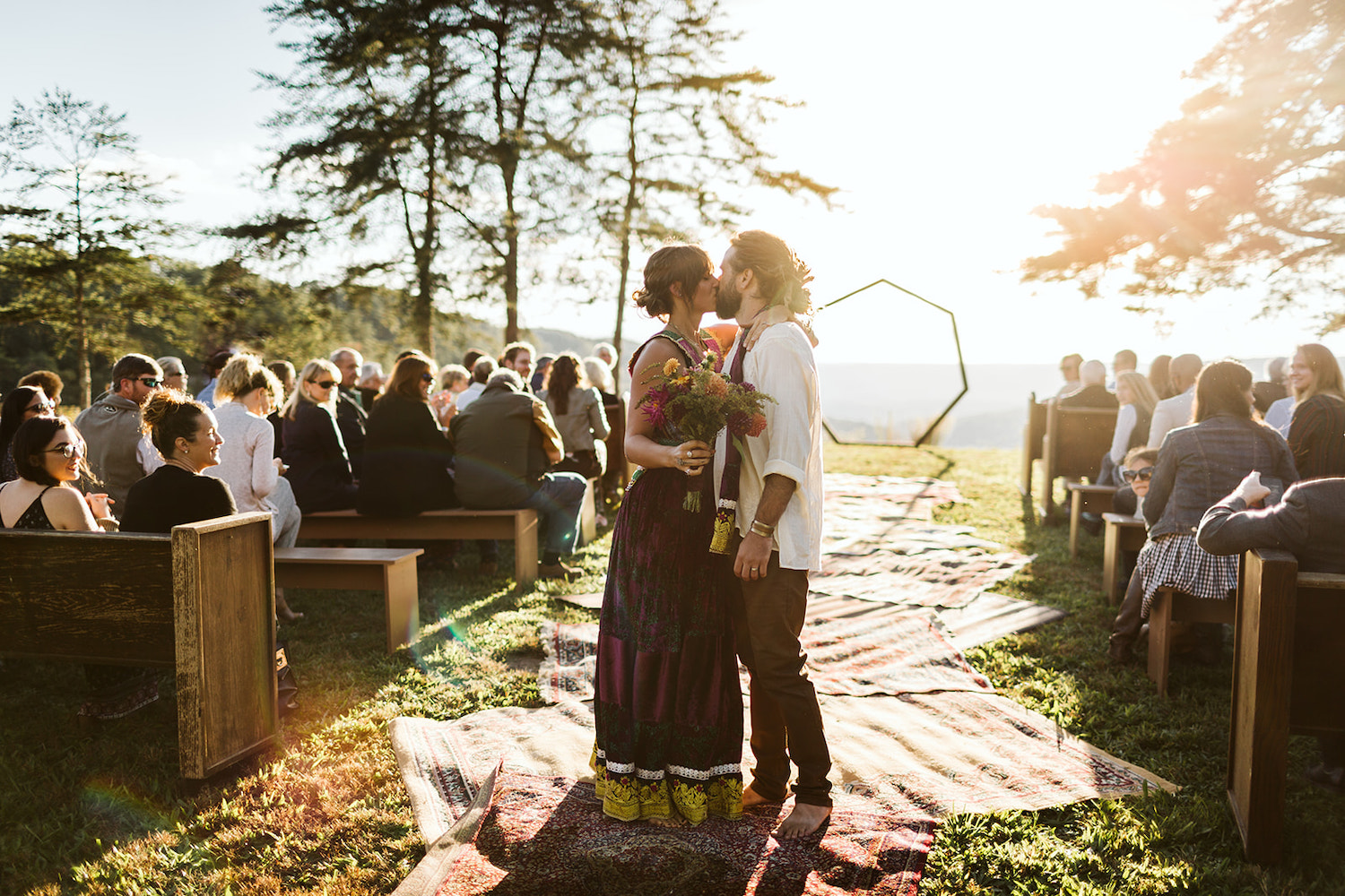 man and woman dressed in Bohemian style kiss on Oriental rug-lined aisle at Hemlock Falls wedding ceremony near Chattanooga