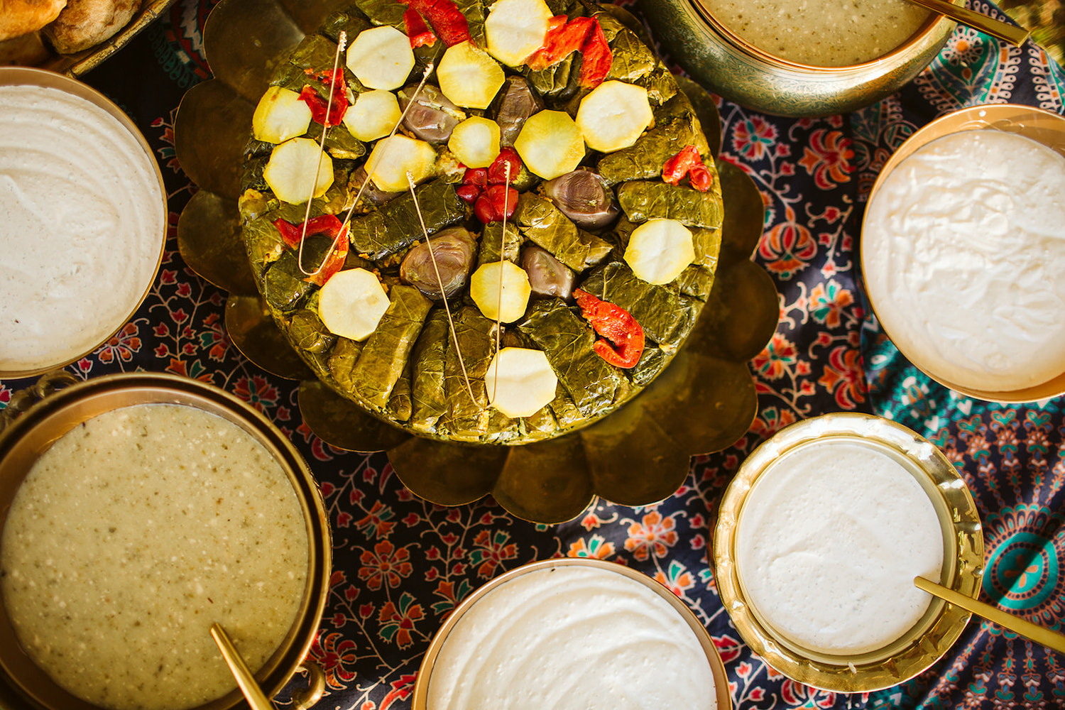 grape leaf wrapped snacks and vegetables on a platter surrounded by various dipping sauces