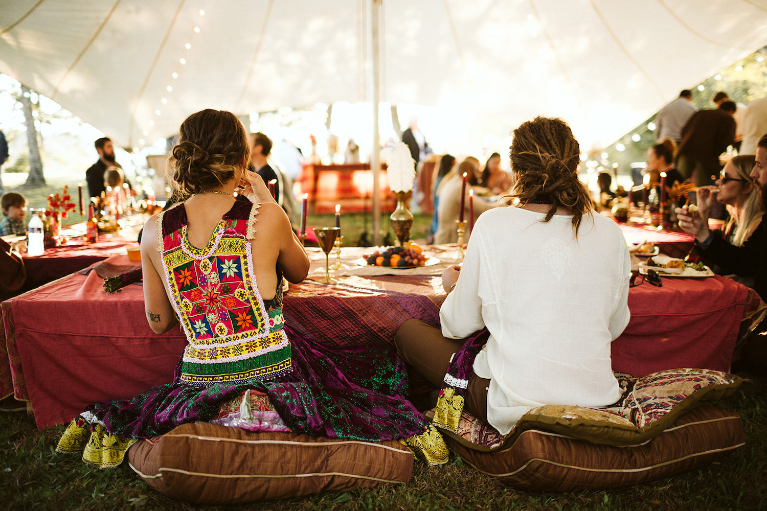 man and woman sit on pillows at a low dining table under a white tent at their Bohemian festival wedding at Hemlock Falls