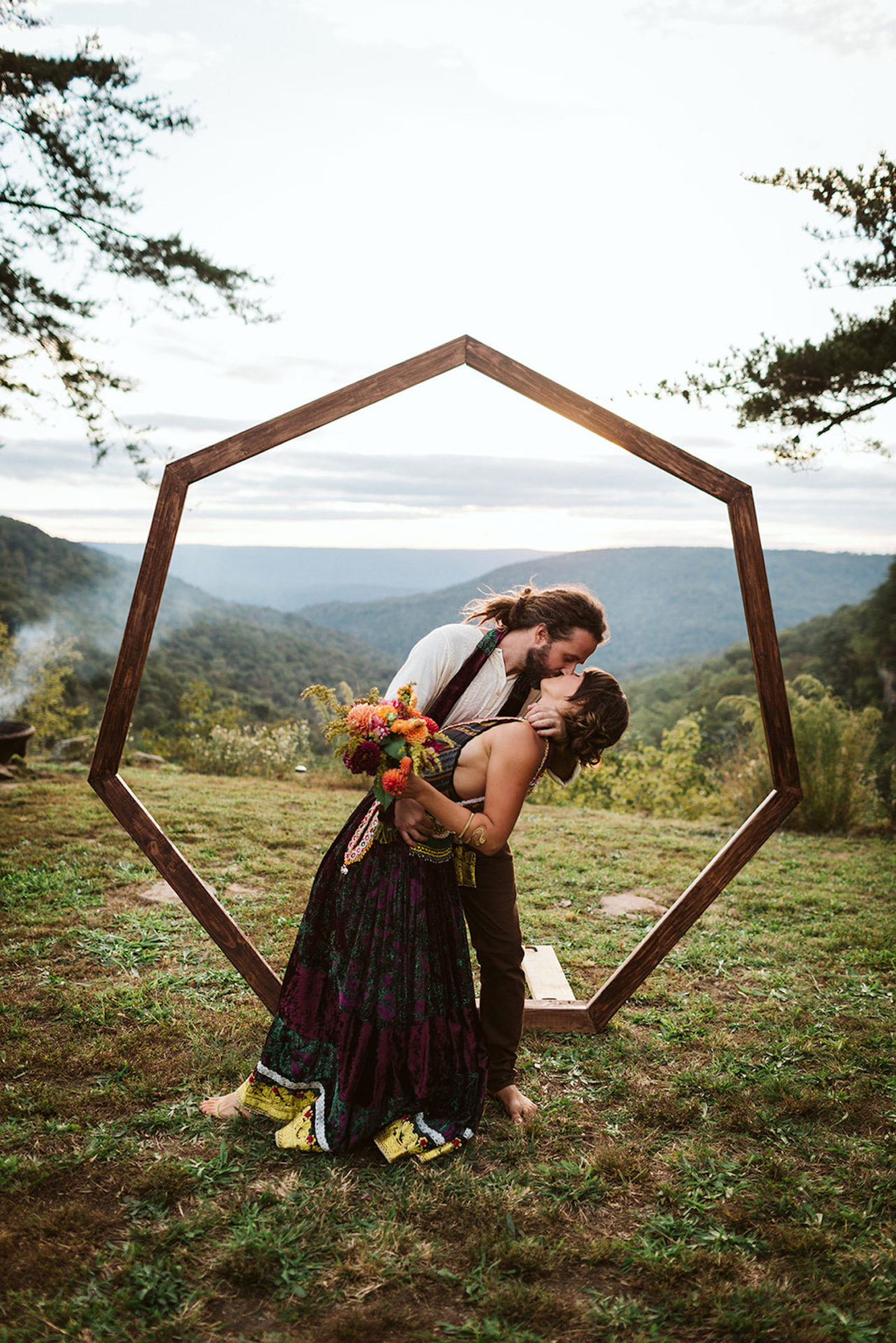 man dips and kisses woman in front of heptagon arch at their Bohemian Festival wedding at Hemlock Falls near Chattanooga