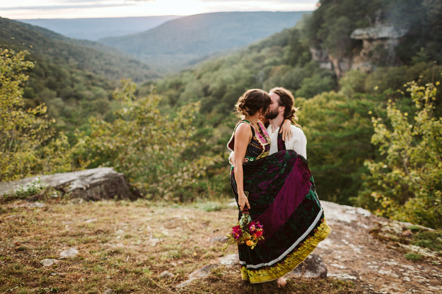 man carries and kisses woman in colorful dress after their Bohemian festival wedding in Chattanooga, Tennessee