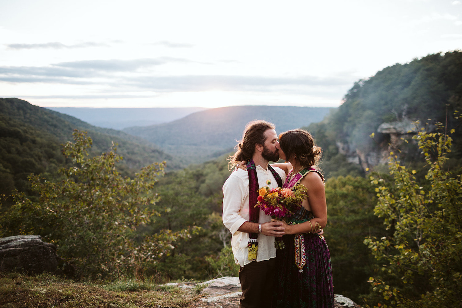 man in white shirt and colorful scarf kisses woman in bright dress at overlook at Hemlock Falls near Chattanooga