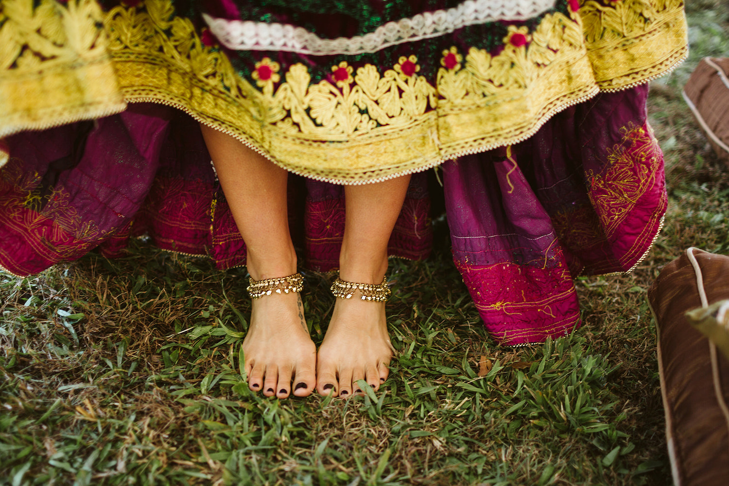 woman lifts front hem of her brightly colored Bohemian wedding dress to show her bare feet and brass anklets