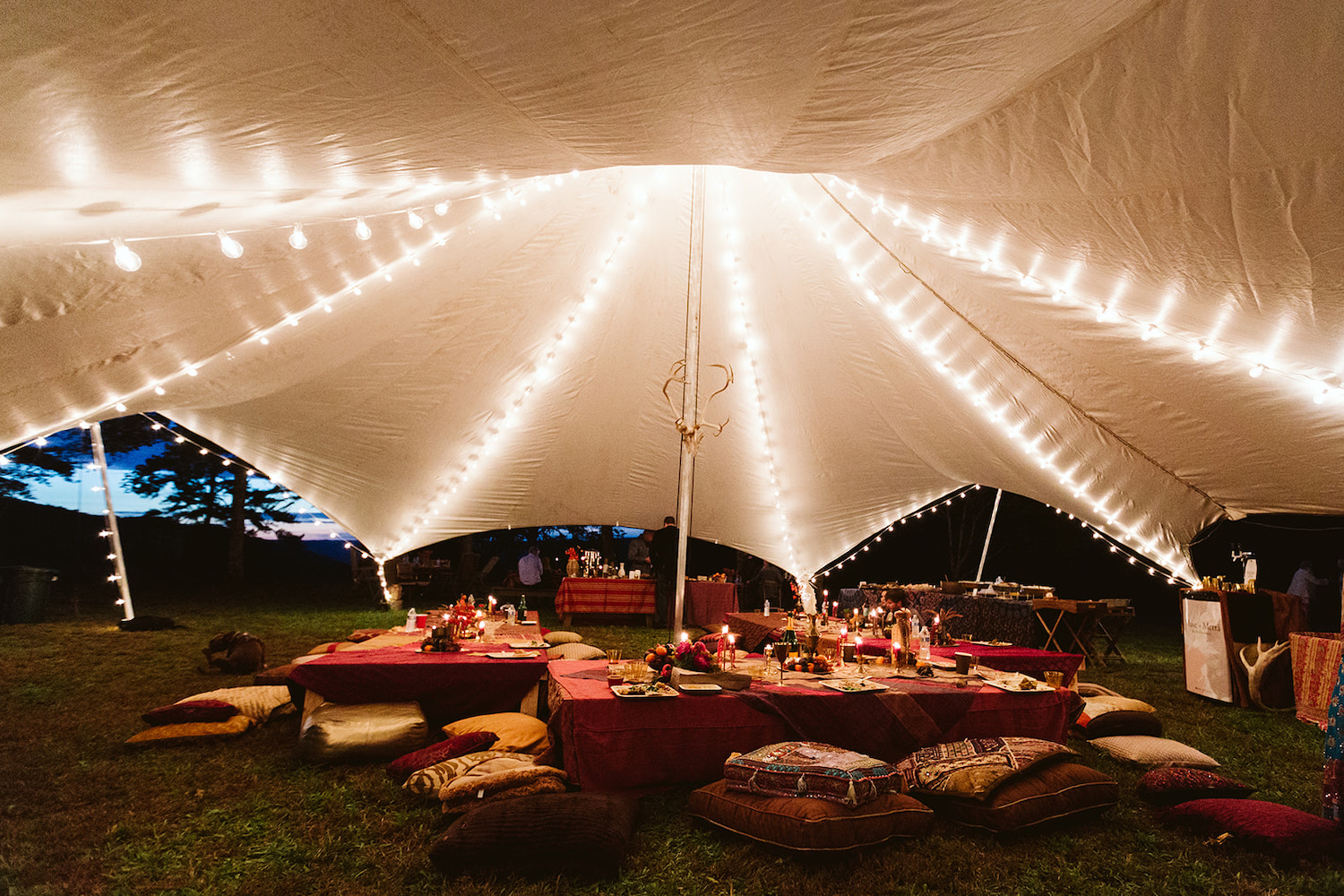 large white tent lit with white string lights over low tables and pillow seating