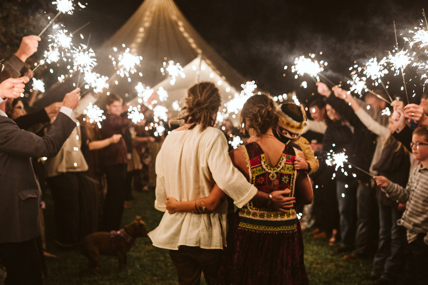 man and woman wearing bright Bohemian gypsy dress walk through sparkler tunnel exit after their Hemlock Falls wedding