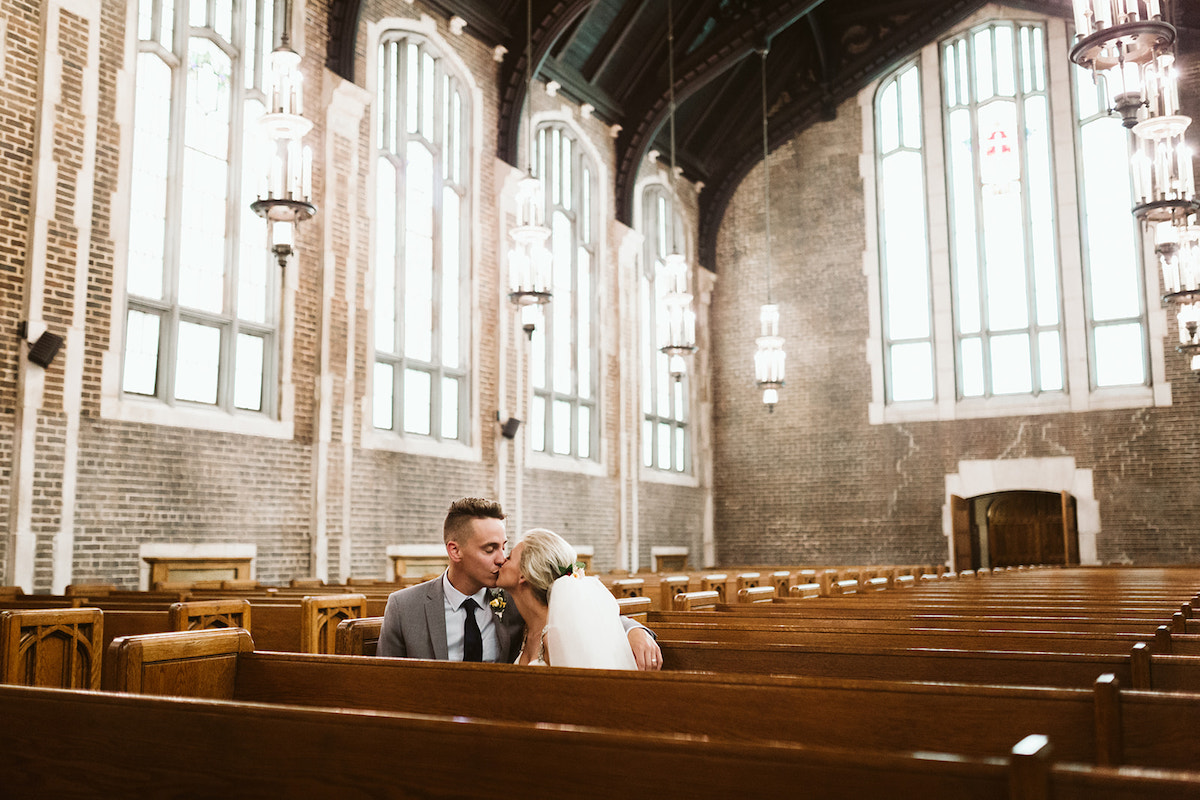 bride and groom kiss in a wooden church pew in an empty brick church sanctuary