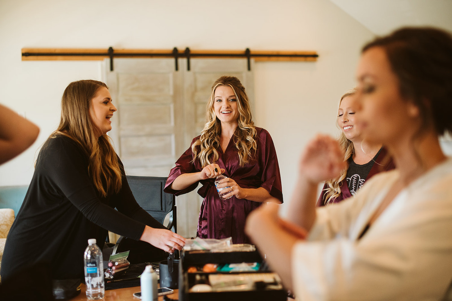 bride and bridesmaids laugh together in high ceiling room with barn doors