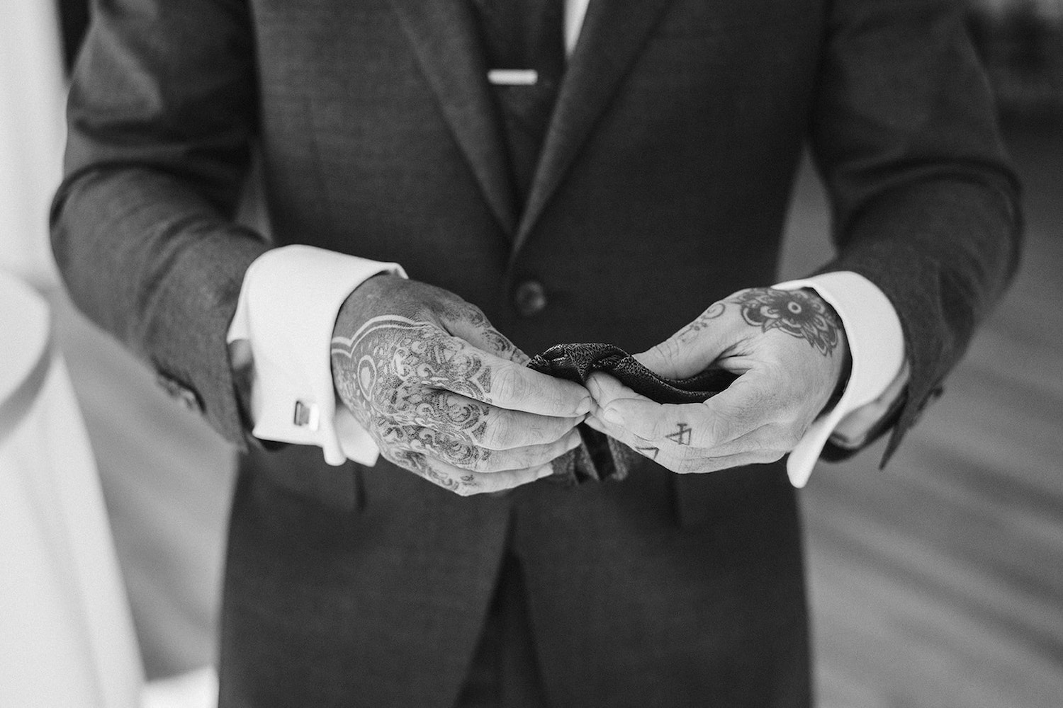 groom's tattoo covered hands fold his pocket square