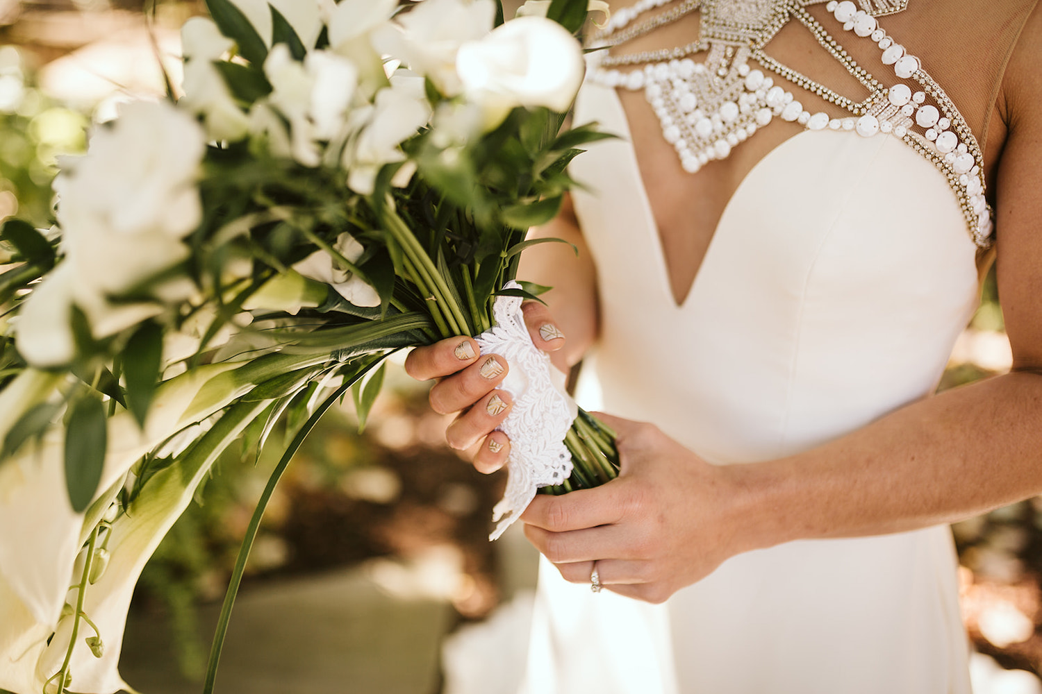 bride holds her bouquet of greenery and white flowers in front of her ornately jeweled bodice