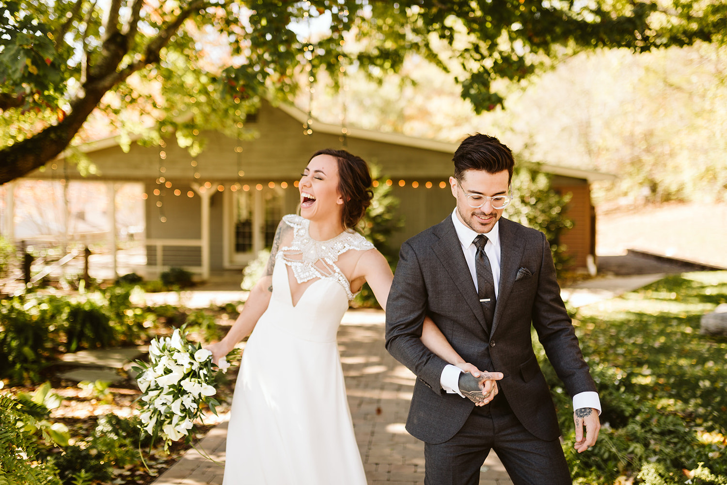 bride laughs while holding hands with groom under large tree