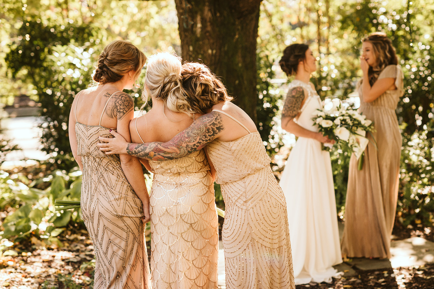 bridesmaids hug each other while bride laughs with another bridesmaid under a large tree