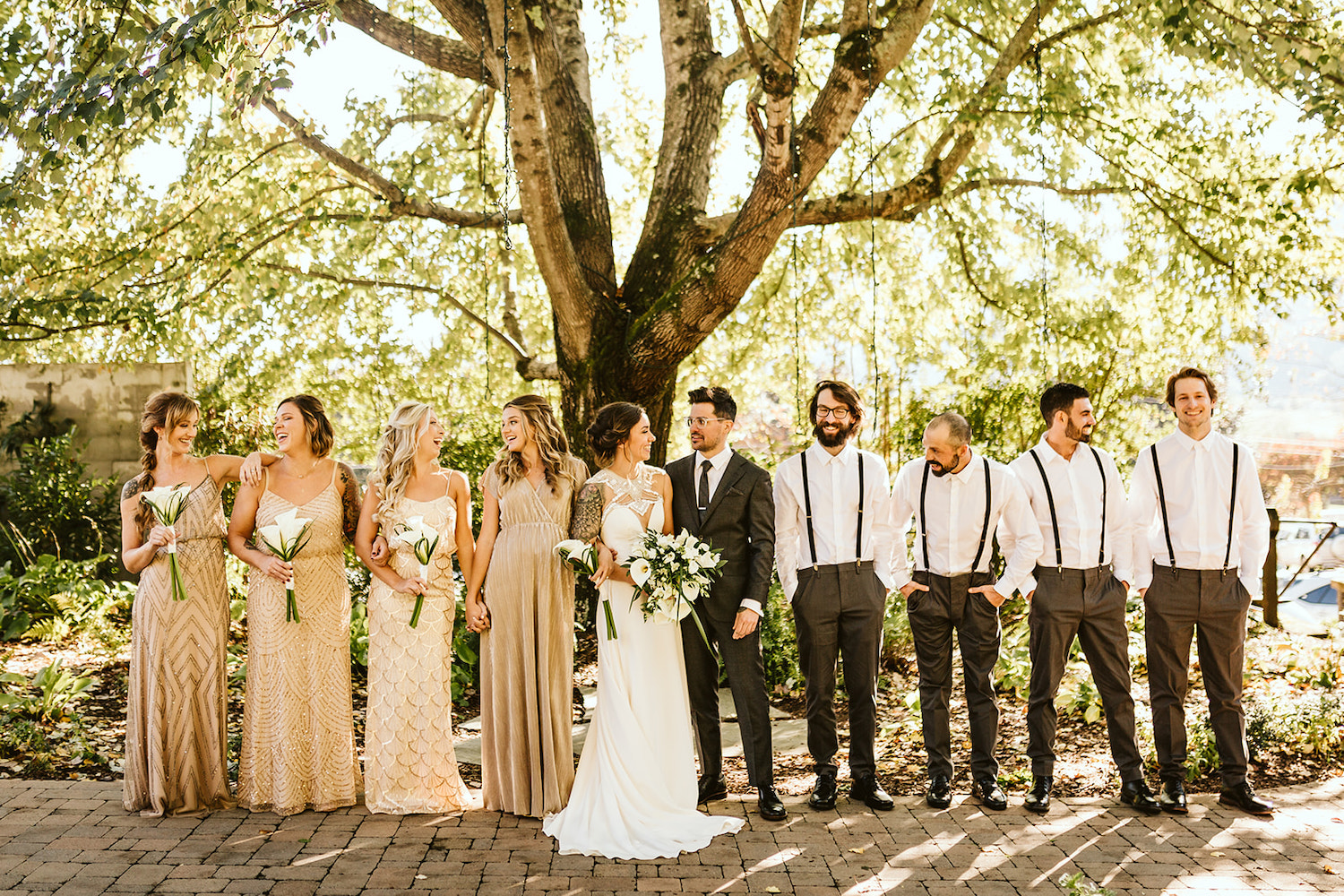 bride and groom stand with wedding party on stone paver path under large tree near Chattanooga, TN