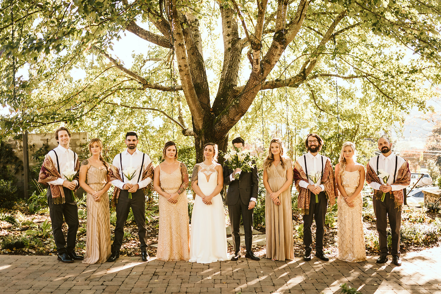 bride and groom stand with wedding party on stone paver path under large tree near Chattanooga, TN