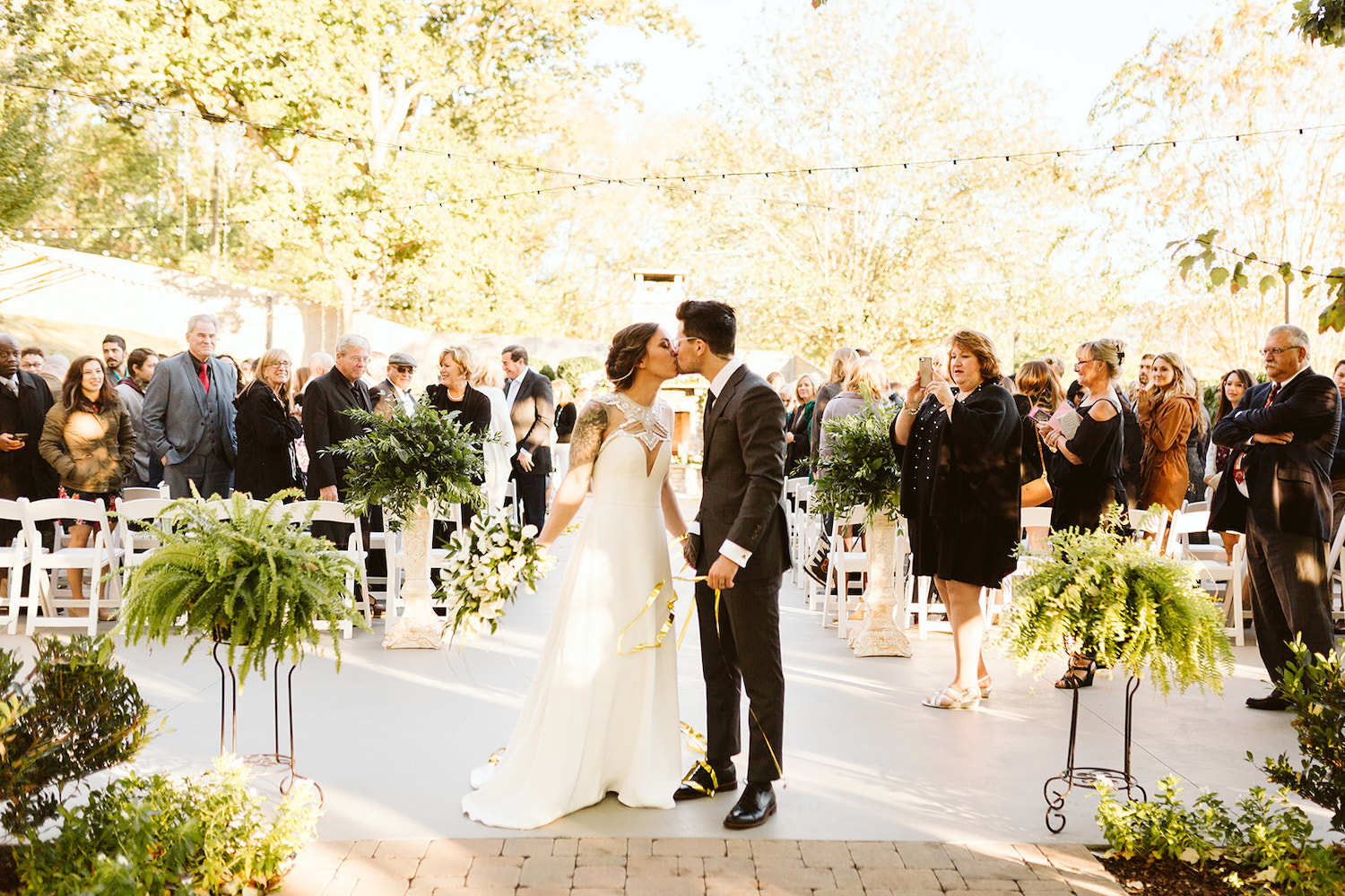 bride and groom kiss at the end of the aisle while guests watch