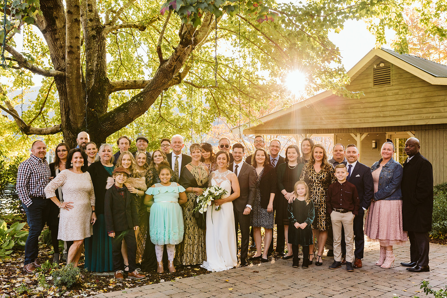 bride and groom pose for family photo under a large tree