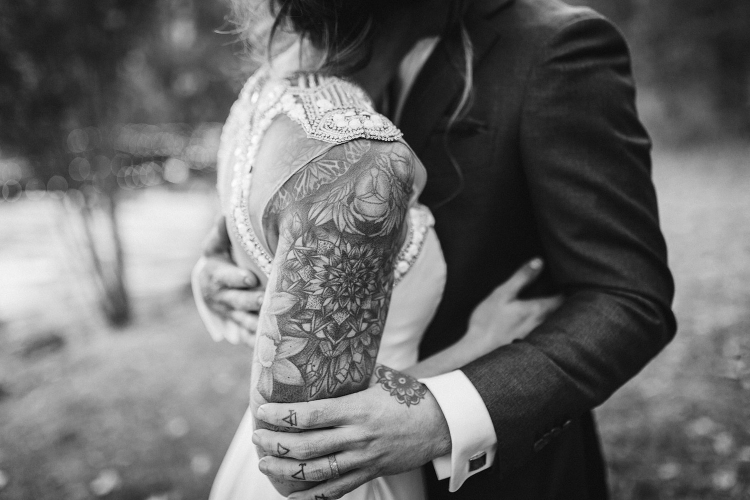 bride and groom hold each other tightly. he grasps her tattooed arm with his tattooed hand.