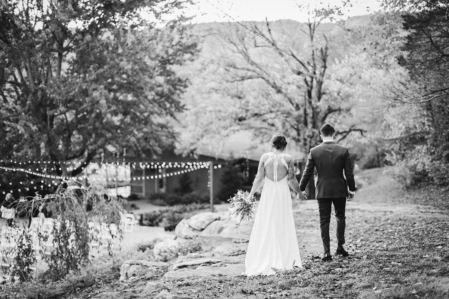 bride and groom hold hands and walk along a grass lawn