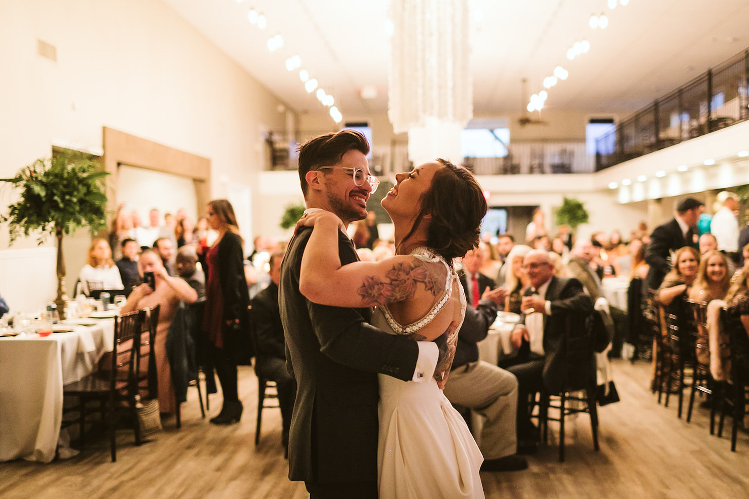bride throws her chin back as she laughs while she and groom dance together as wedding guests watch