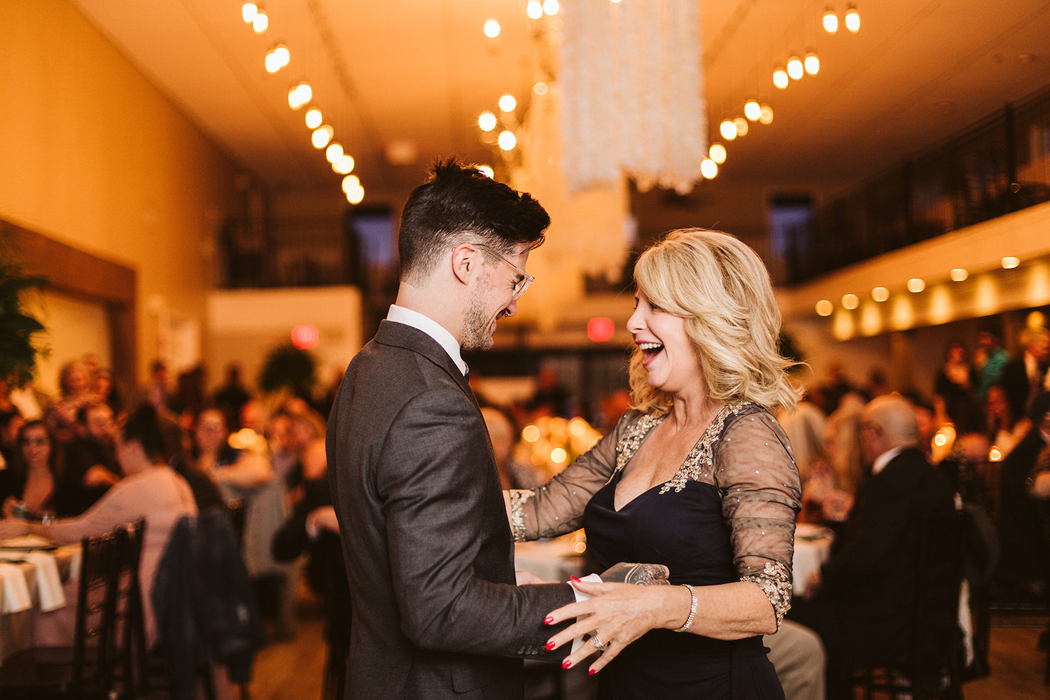 mother of the groom laughs as he reaches toward her during their dance together