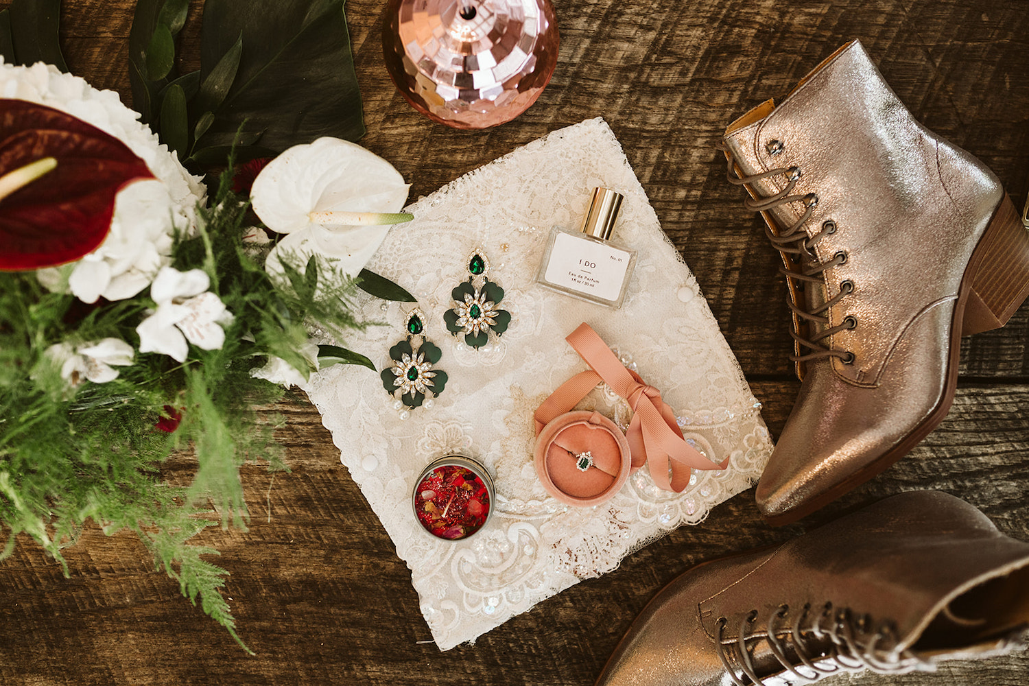 sparkly pink ankle boots sit next to lace square laid with emerald ring and floral earrings