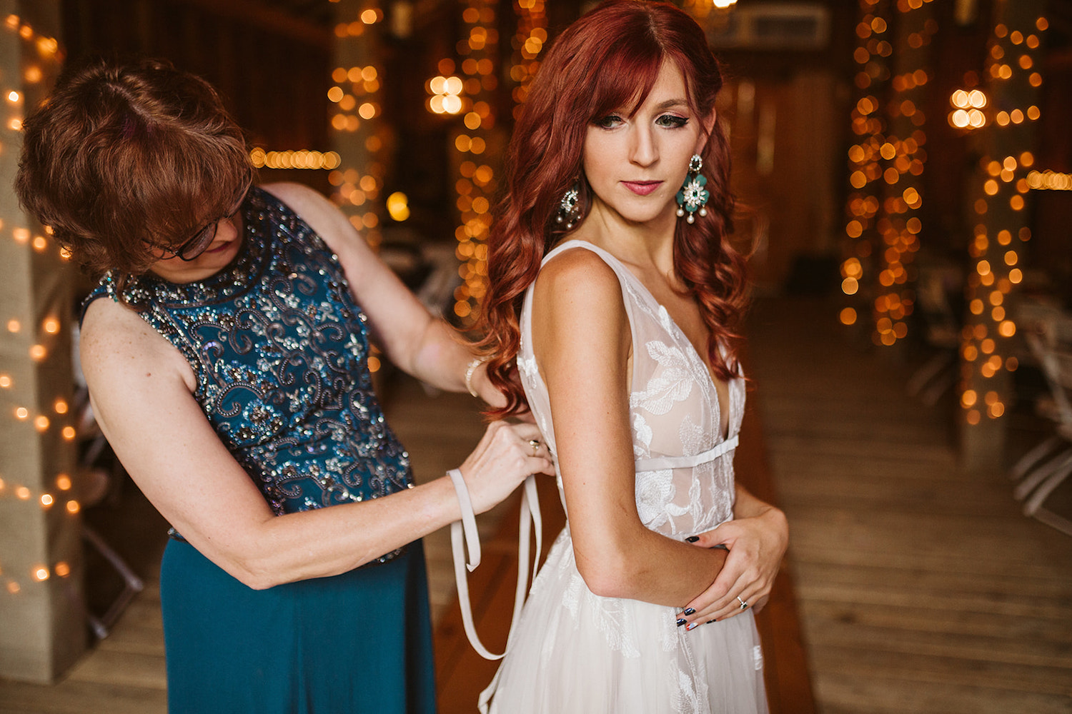 bride crosses her arms in front of her while her mother ties the back of her dress