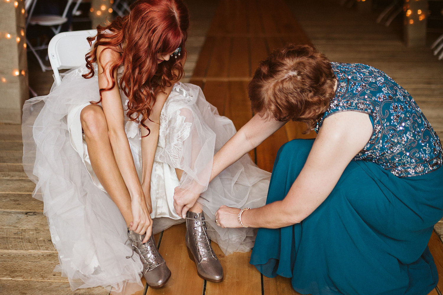 bride puts on lace-up sparkly boots while her mother helps tie them