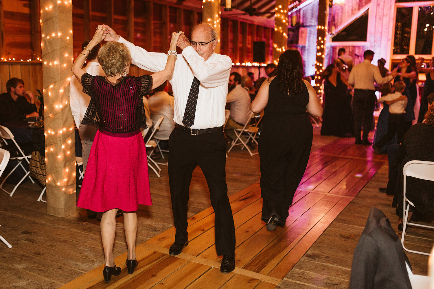 older couple dances under white string lights at wedding reception