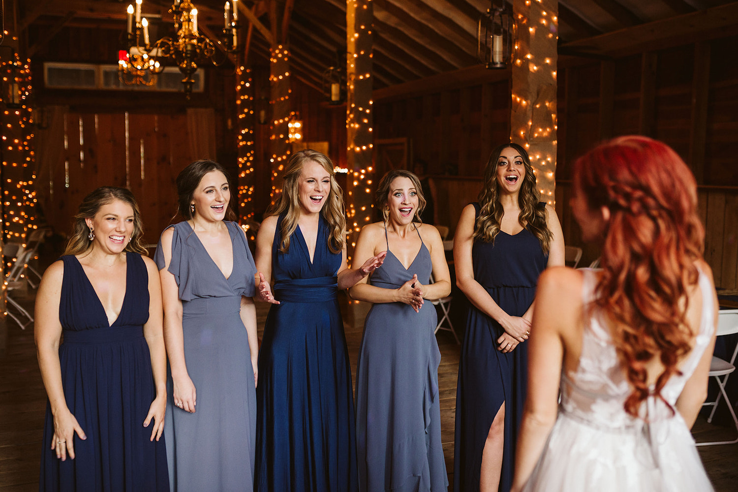 bridesmaids in sleeveless blue dresses react with excitement at their first view of the bride
