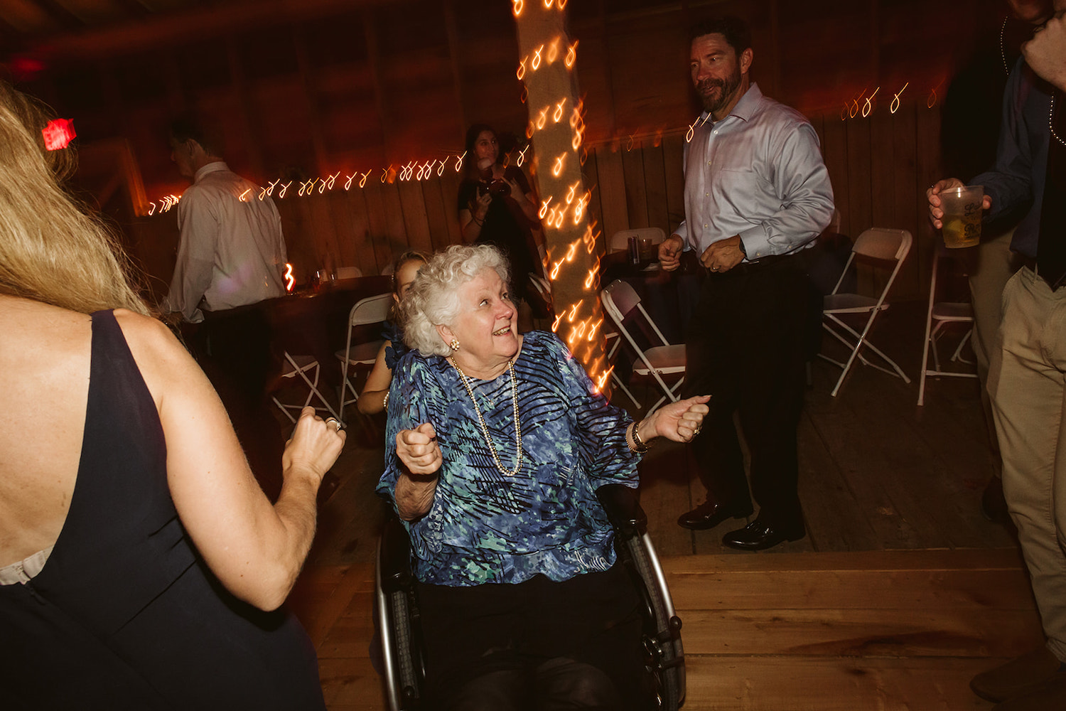 older woman wearing Mardi Gras beads around her neck dances from her wheelchair