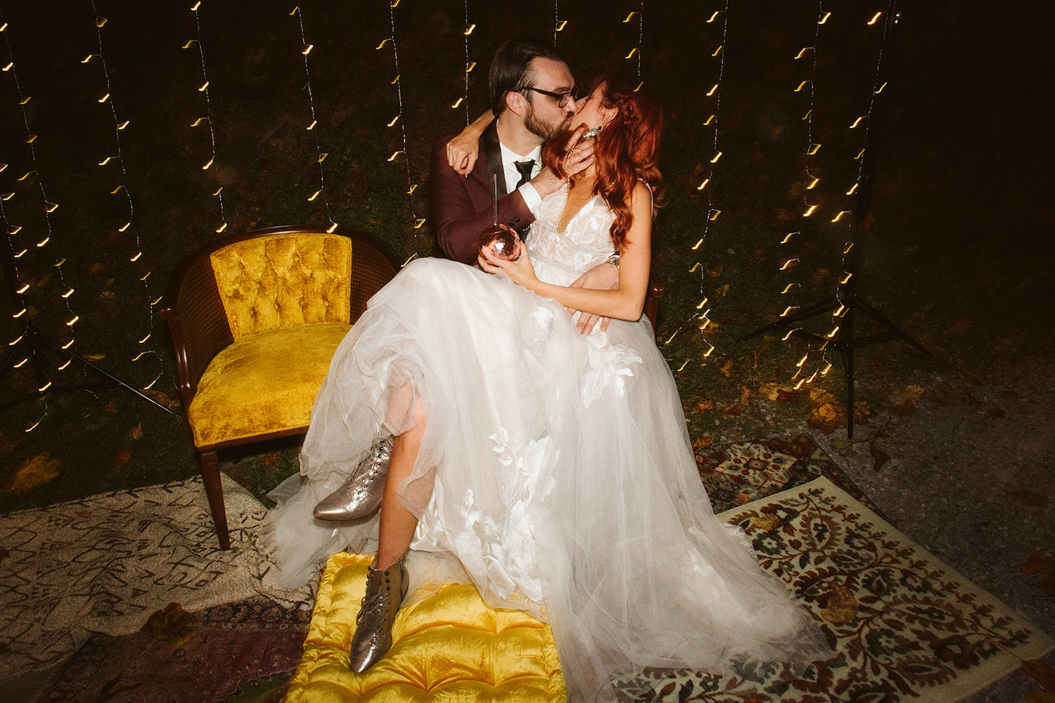 bride sits on grooms lap on a golden antique chair as he kisses her
