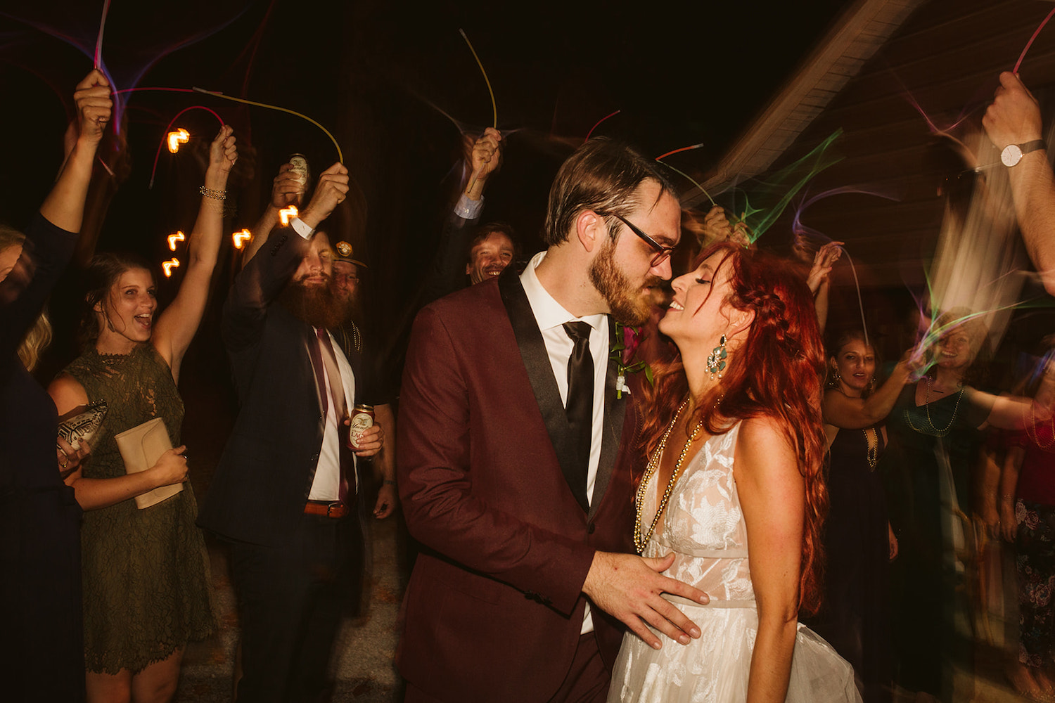 groom and bride start to kiss while wedding guests wave glow sticks around them