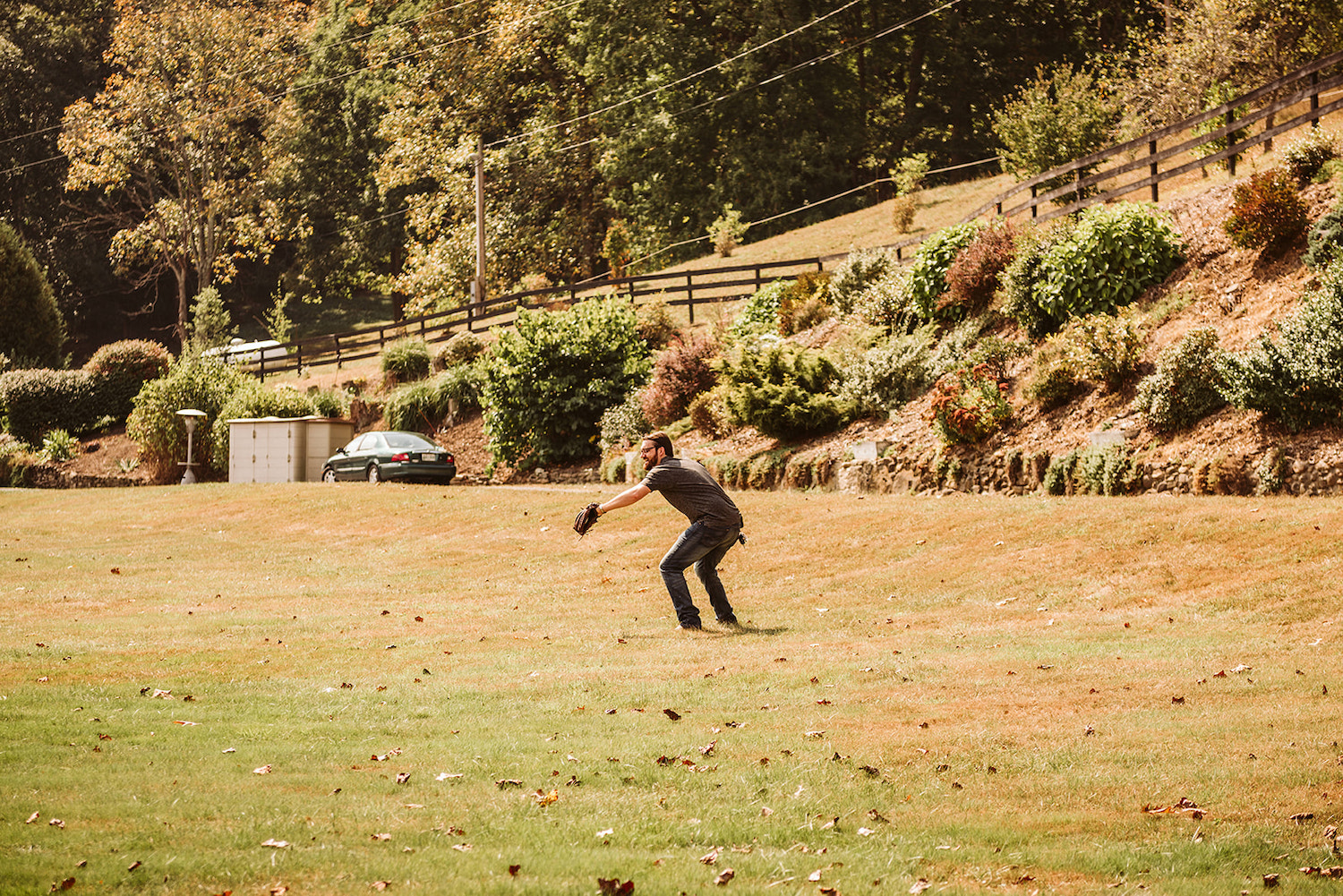 man crouches in field with his baseball-gloved hand extended