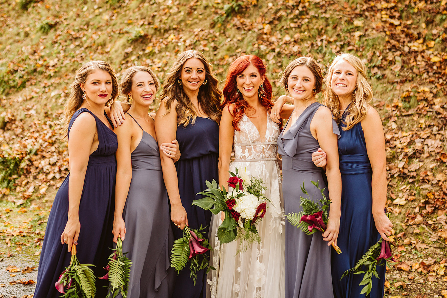 bride and bridesmaids in various blue satin gowns stand with their flowers at their sides