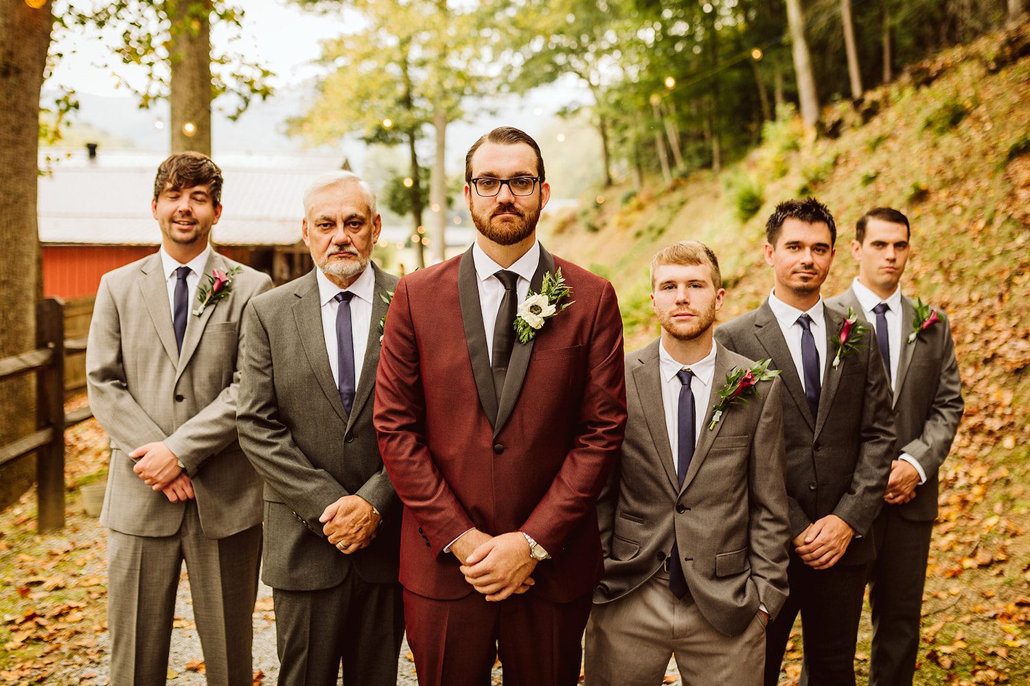 Groom in maroon suit and groomsmen in gray suits stand in a V-formation