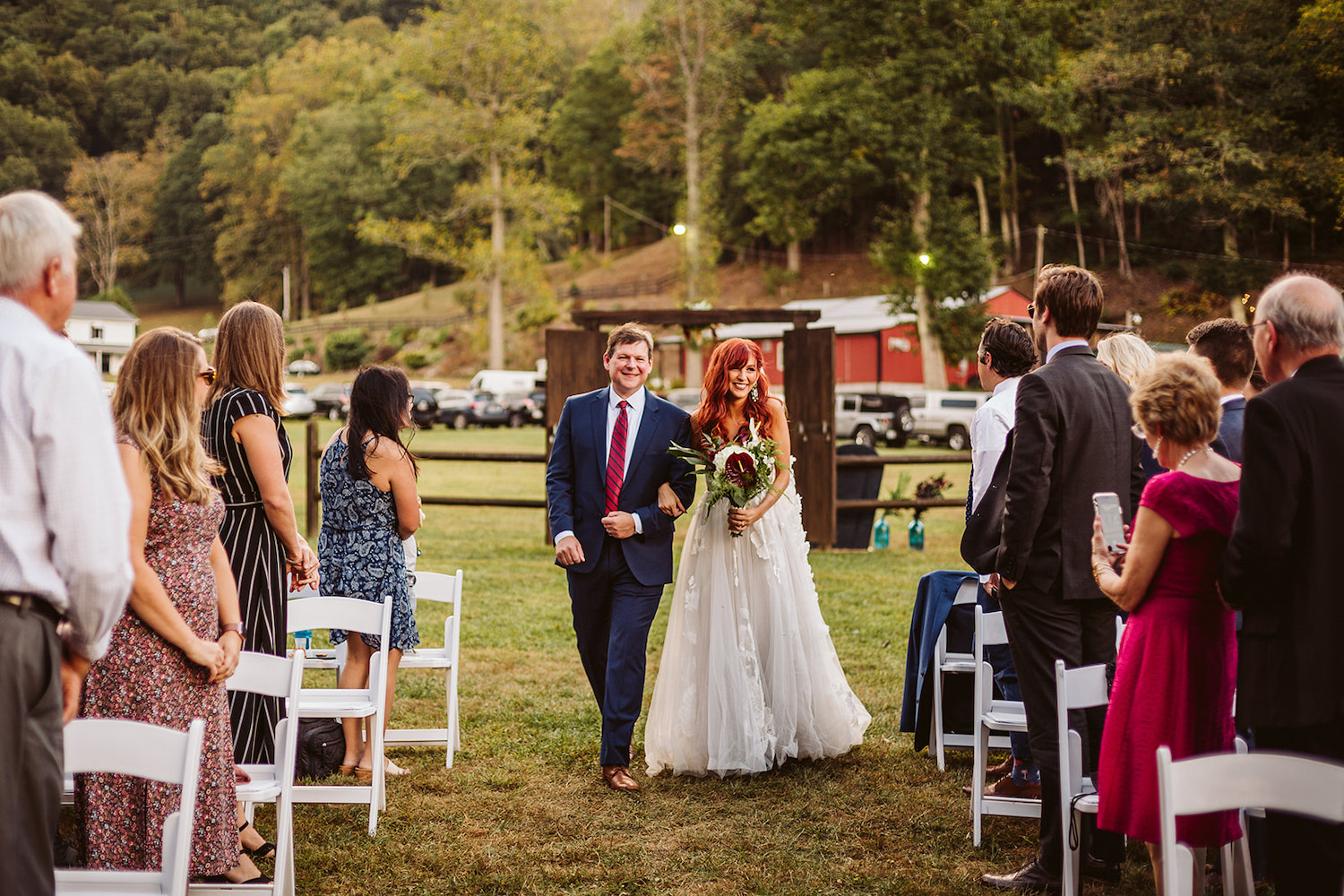 bride walks through wooden doorway in a field toward wedding guests
