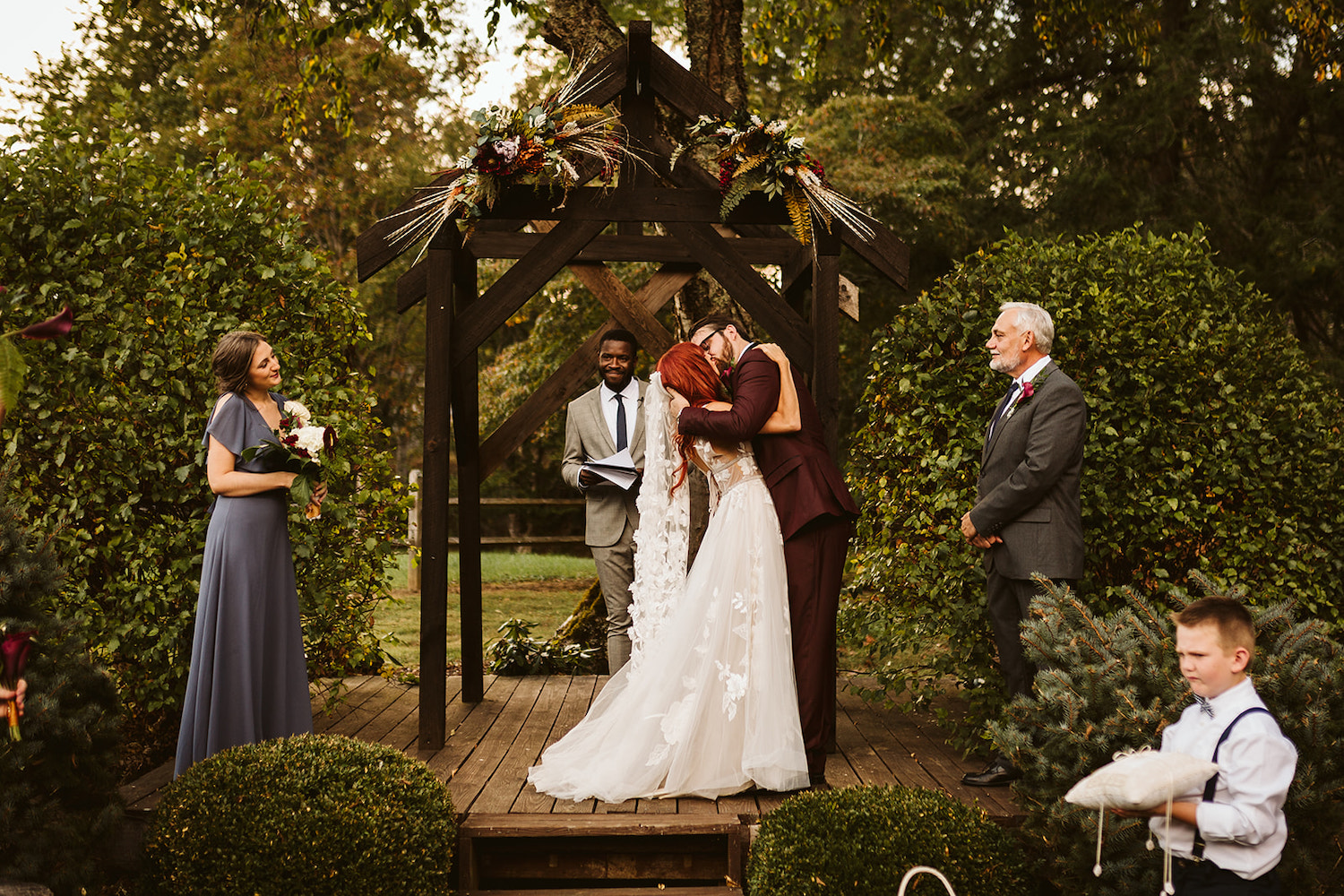 bride and groom kiss while maid of honor, best man, and officiant smile