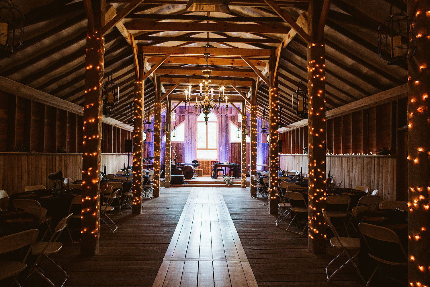 interior barn reception hall with exposed rafters and beams strung with white lights and a candelabra