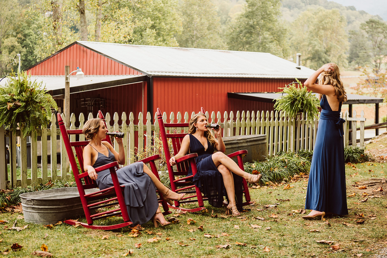 bridesmaids sit in large red rocking chairs drinking beer from bottles