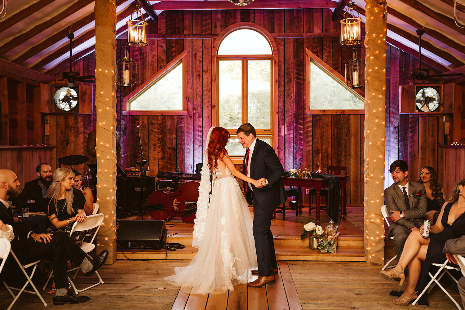 bride and her father dance under exposed beams and rafters while wedding guests watch