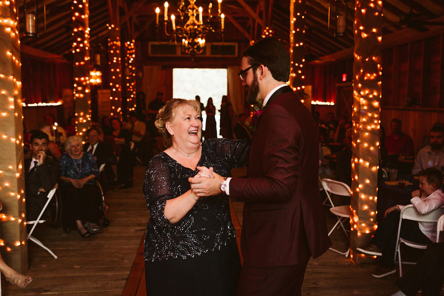 groom and his mother dance under exposed beams and rafters while wedding guests watch