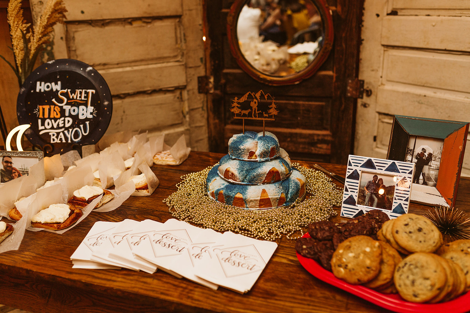 table decorated with hand painted signs and mardi gras beads around cinnamon buns, cookings, and cake