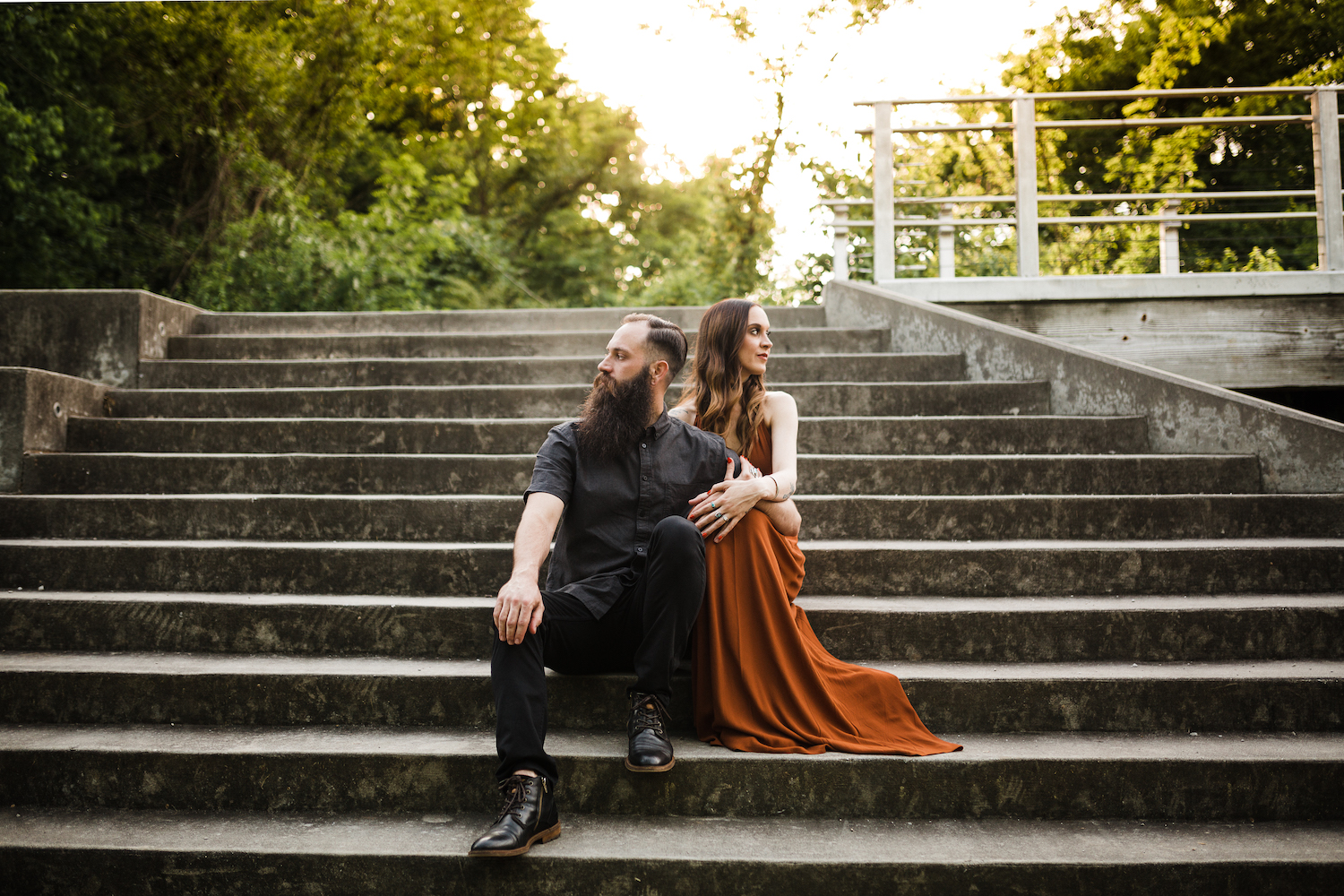 man in all black and woman in amber satin dress sit on cement steps of Chattanooga's Renaissance Park near downtown
