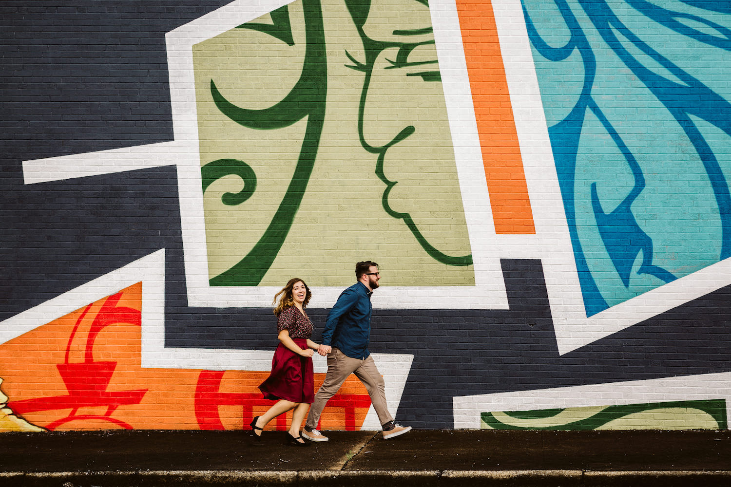 man and woman hold hands and run across a vibrantly painted wall in downtown Chattanooga, Tennessee