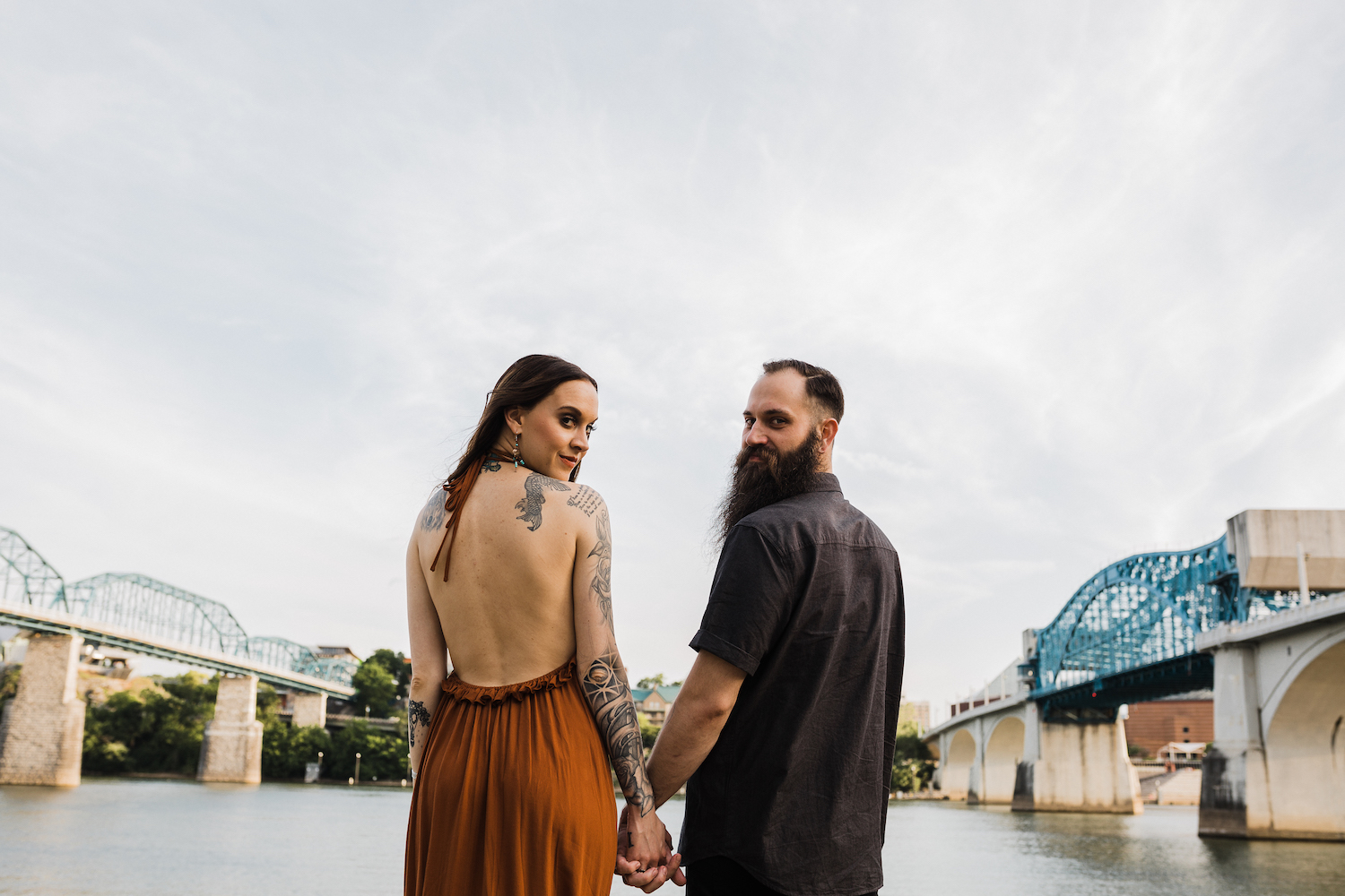 man and woman hold hands in Chattanooga's Coolidge Park between views of Market Street and Walnut Street Bridges