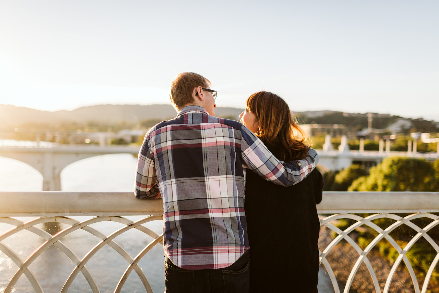 man and woman cuddle on Chattanooga's Walnut Street Walking Bridge as the sun sets